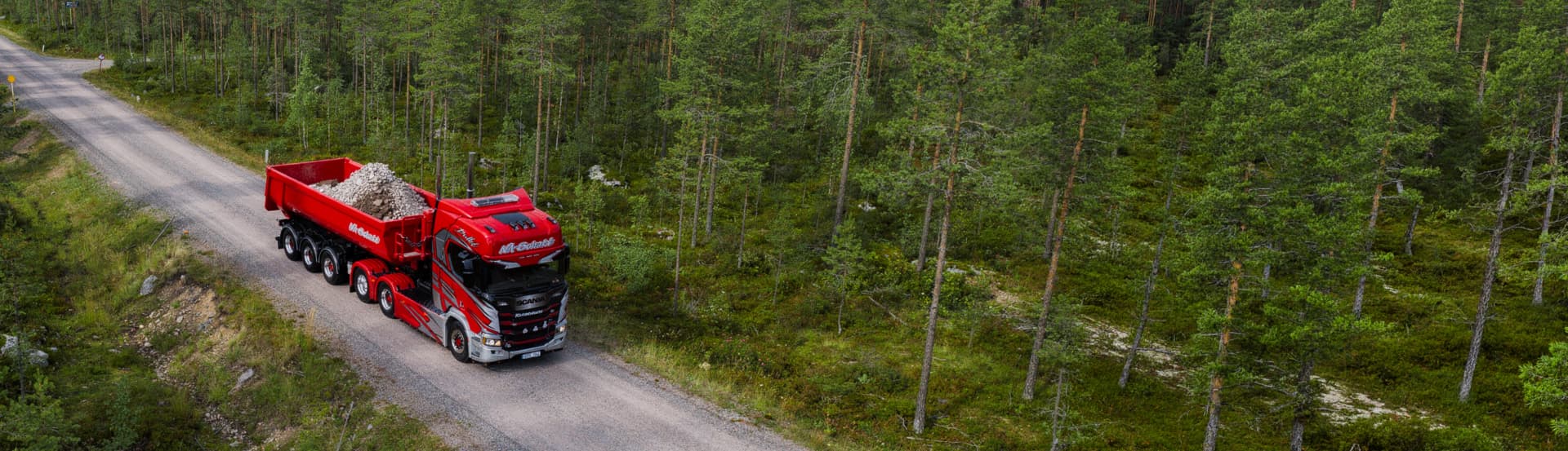 Röd lastbil med grus på skogsväg sedd uppifrån